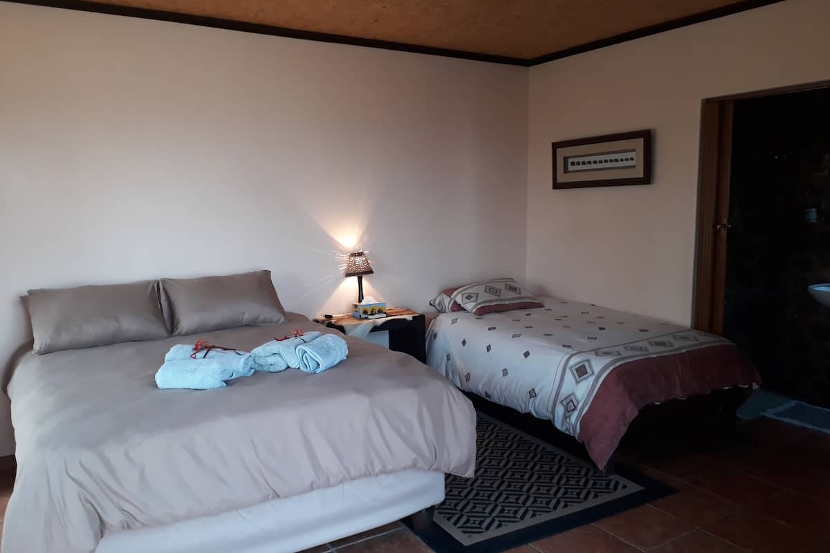 Un dormitorio con una cama grande, otra más pequeña, una mesita de noche con lámpara y un cuadro enmarcado en la pared.