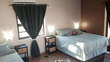 A bedroom with a bed, two nightstands, a window with curtains, and a wall-mounted air conditioner.