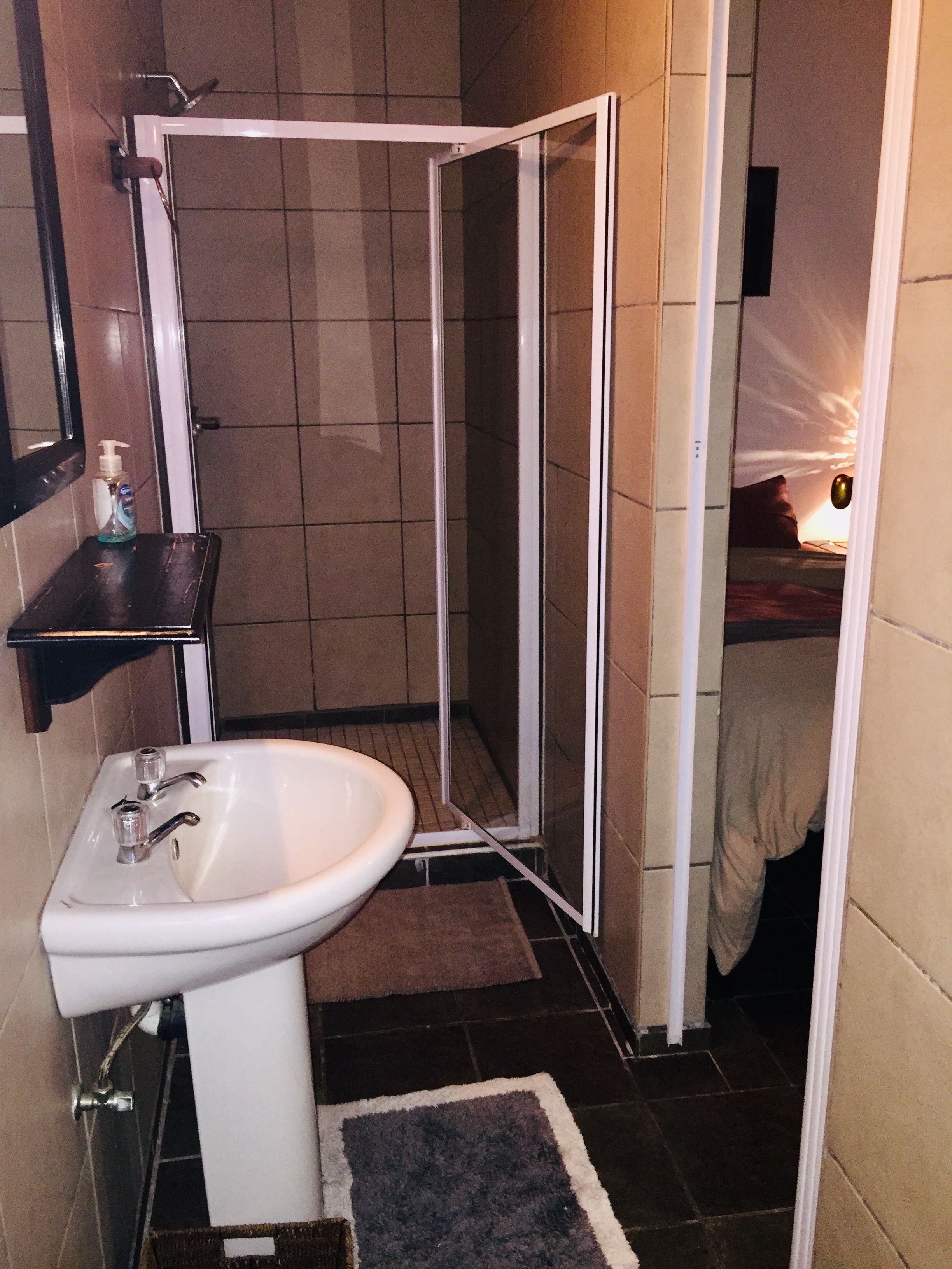 Een badkamer met een wit wastafelmeubel, een douchecabine en een klein plankje met een fles.