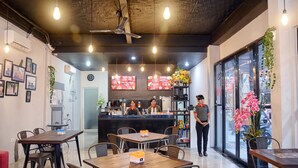 Un café moderno con mesas y sillas de madera, una barra con carteles de menú y un ventilador de techo.