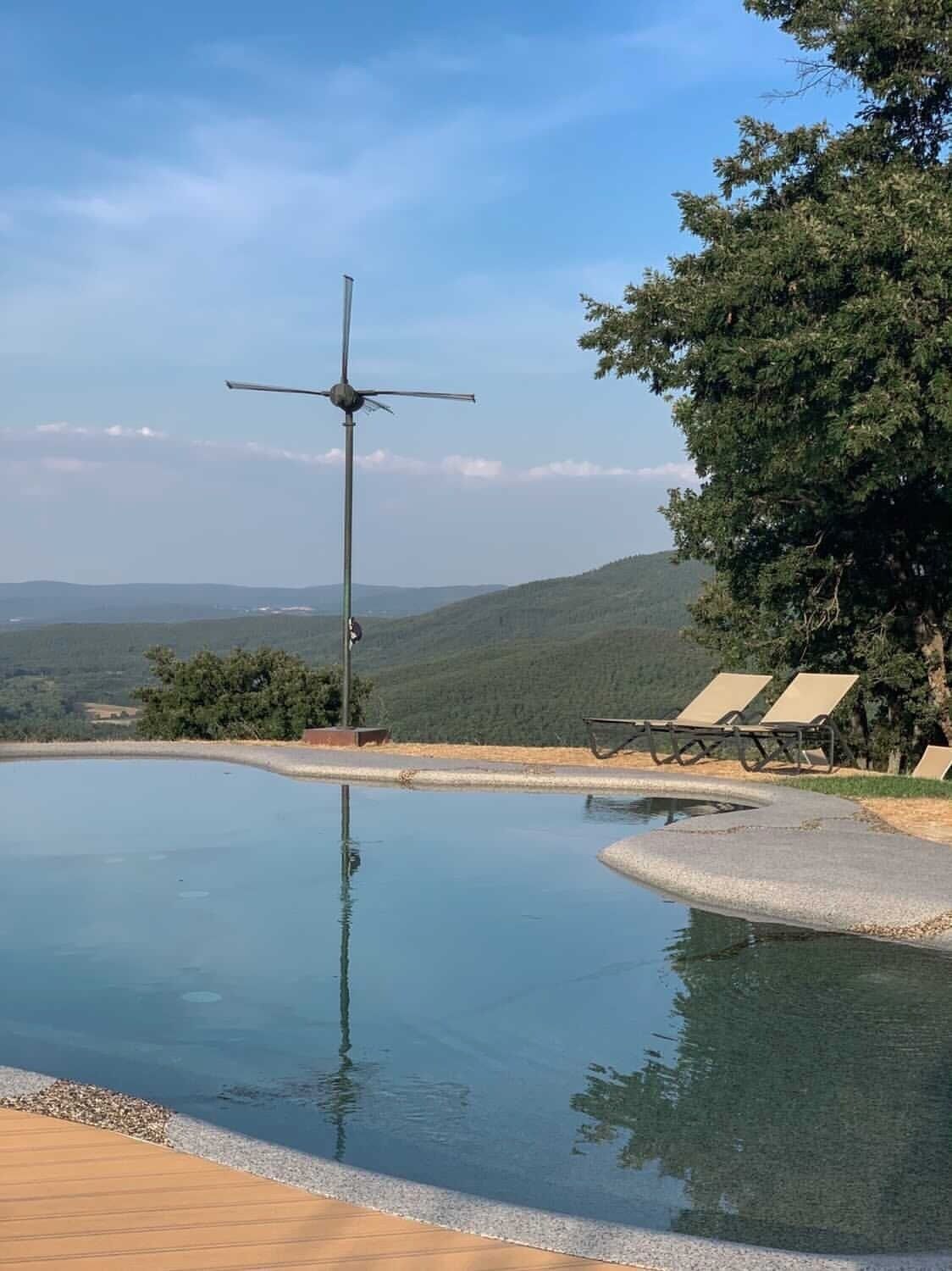 Una piscina con una turbina eólica, sillas de descanso y vistas a las colinas.