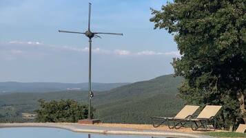 Una piscina con una turbina eólica, sillas de descanso y vistas a las colinas.