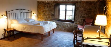 A bedroom with a bed, a desk with a chair, a ceiling fan, and a stone wall.