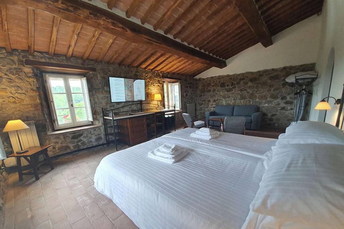 A bedroom with a large bed, a desk, a chair, a sofa, and a stone wall.
