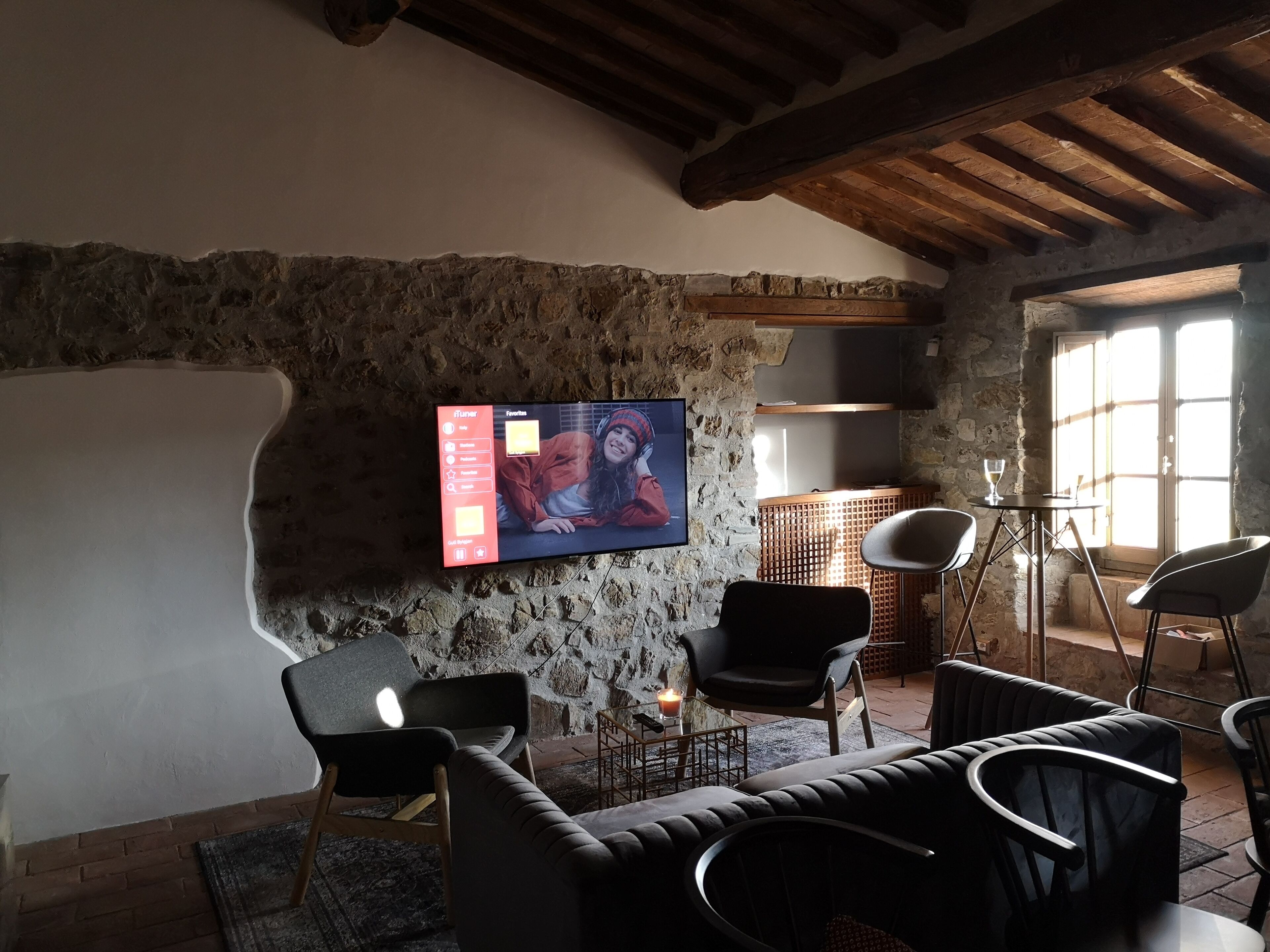 A cozy room with a stone wall, a flat-screen TV mounted on it, and a seating area with modern chairs and a sofa.