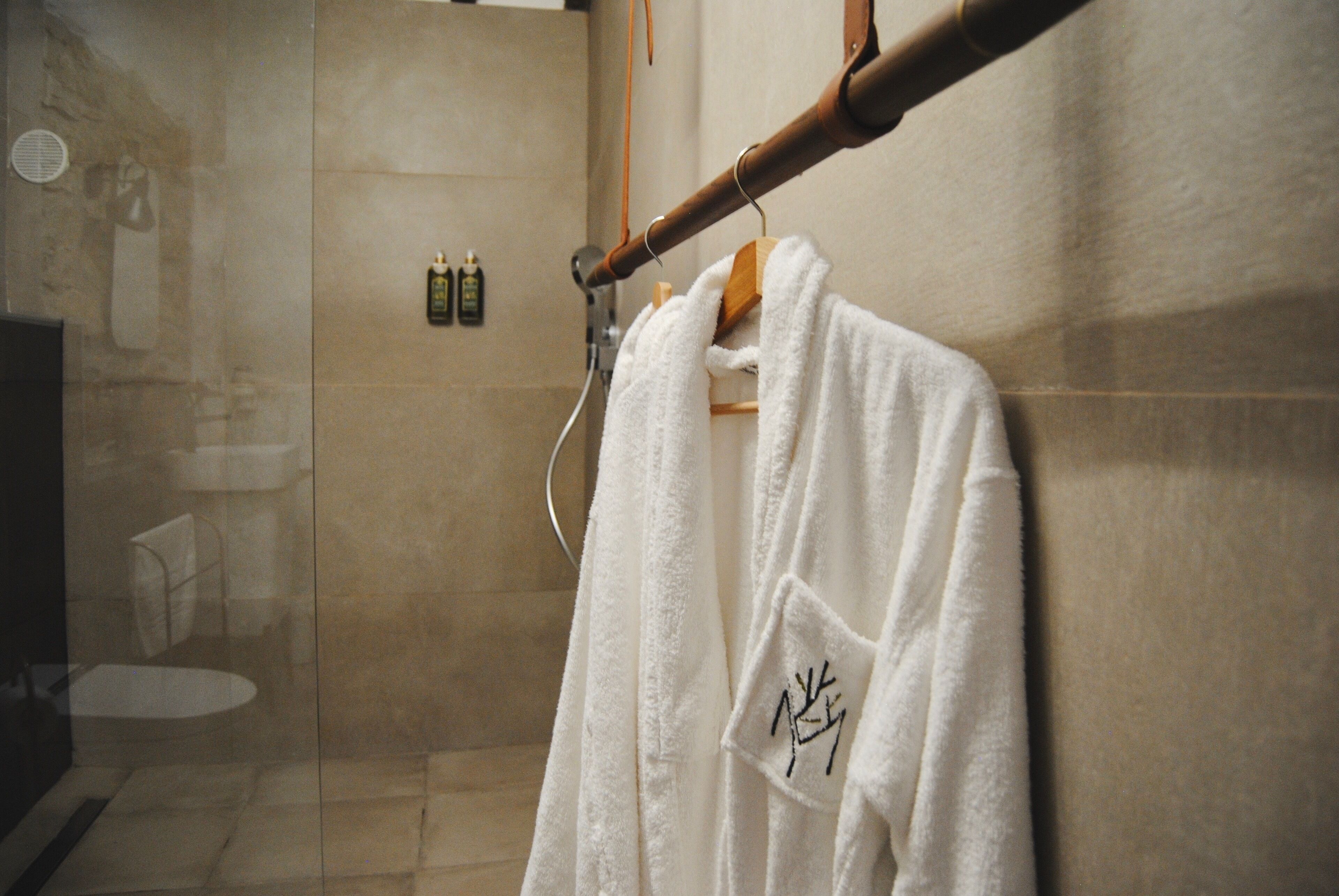A white towel hanging on a wooden rack in a bathroom with a tiled wall and a glass shower door.