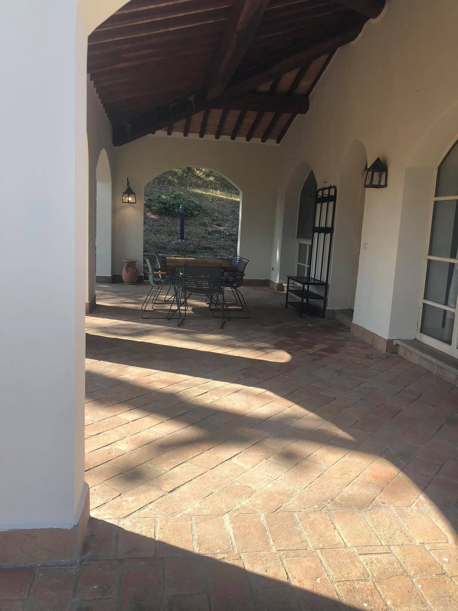 Uma área de pátio ao ar livre com piso de tijolos, uma mesa de madeira com cadeiras e vista para uma encosta.