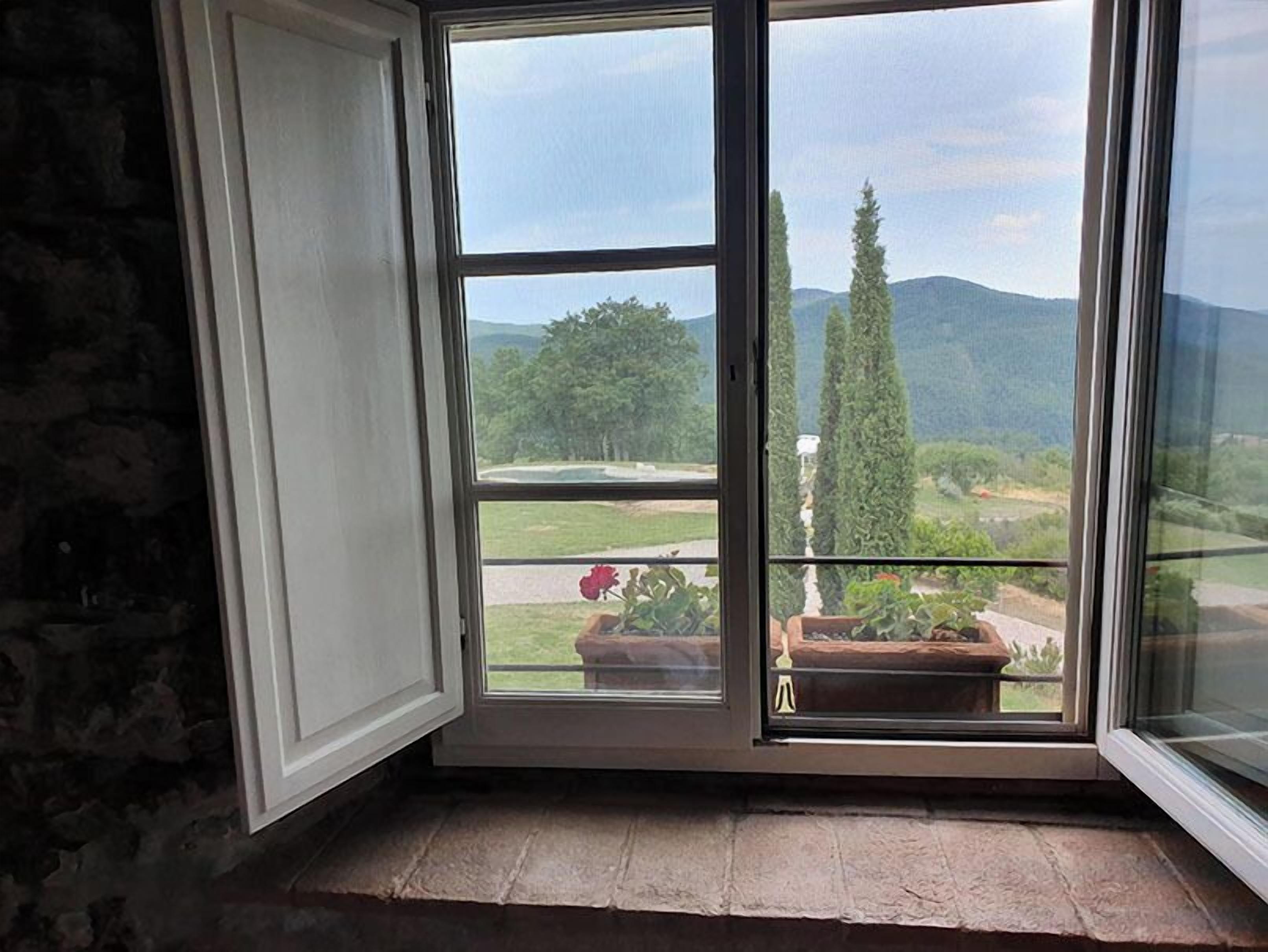 Una habitación con un ventanal grande que da a un paisaje pintoresco con árboles y colinas.