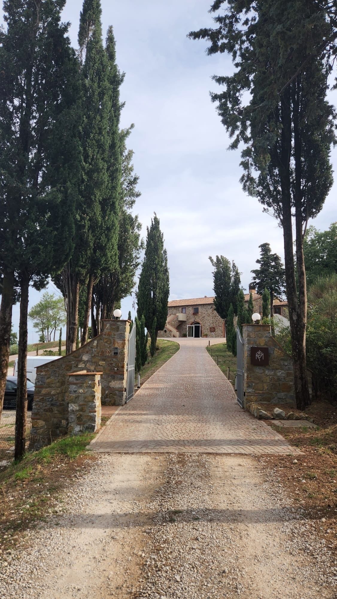 Un chemin de pierres mène à un bâtiment rustique doté d’un toit en tuiles, entouré de grands arbres.