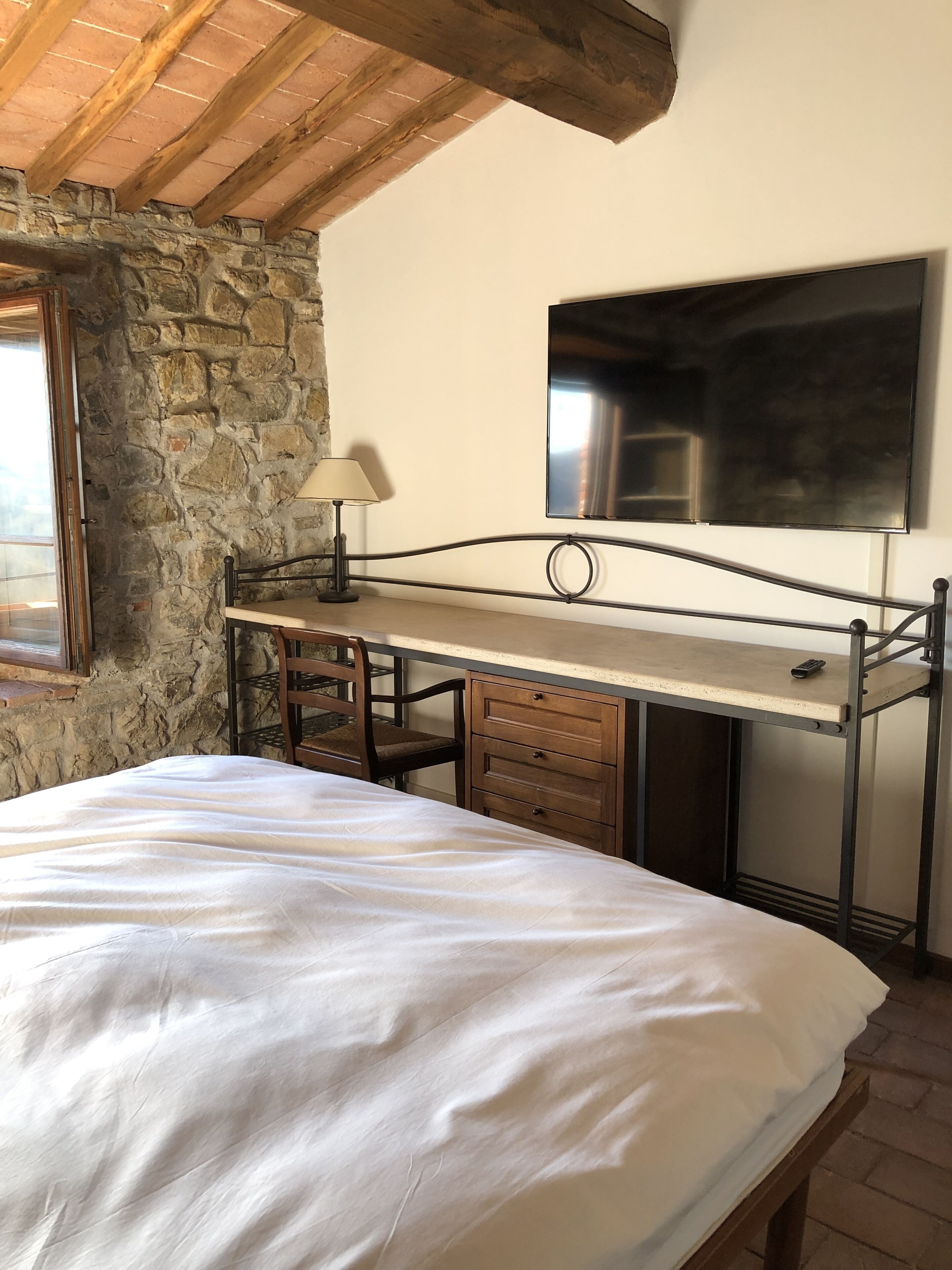 Une chambre à coucher avec un lit, un bureau, une chaise, une lampe, une télévision et un mur en pierre.