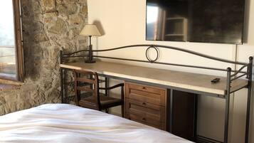 Une chambre à coucher avec un lit, un bureau, une chaise, une lampe, une télévision et un mur en pierre.