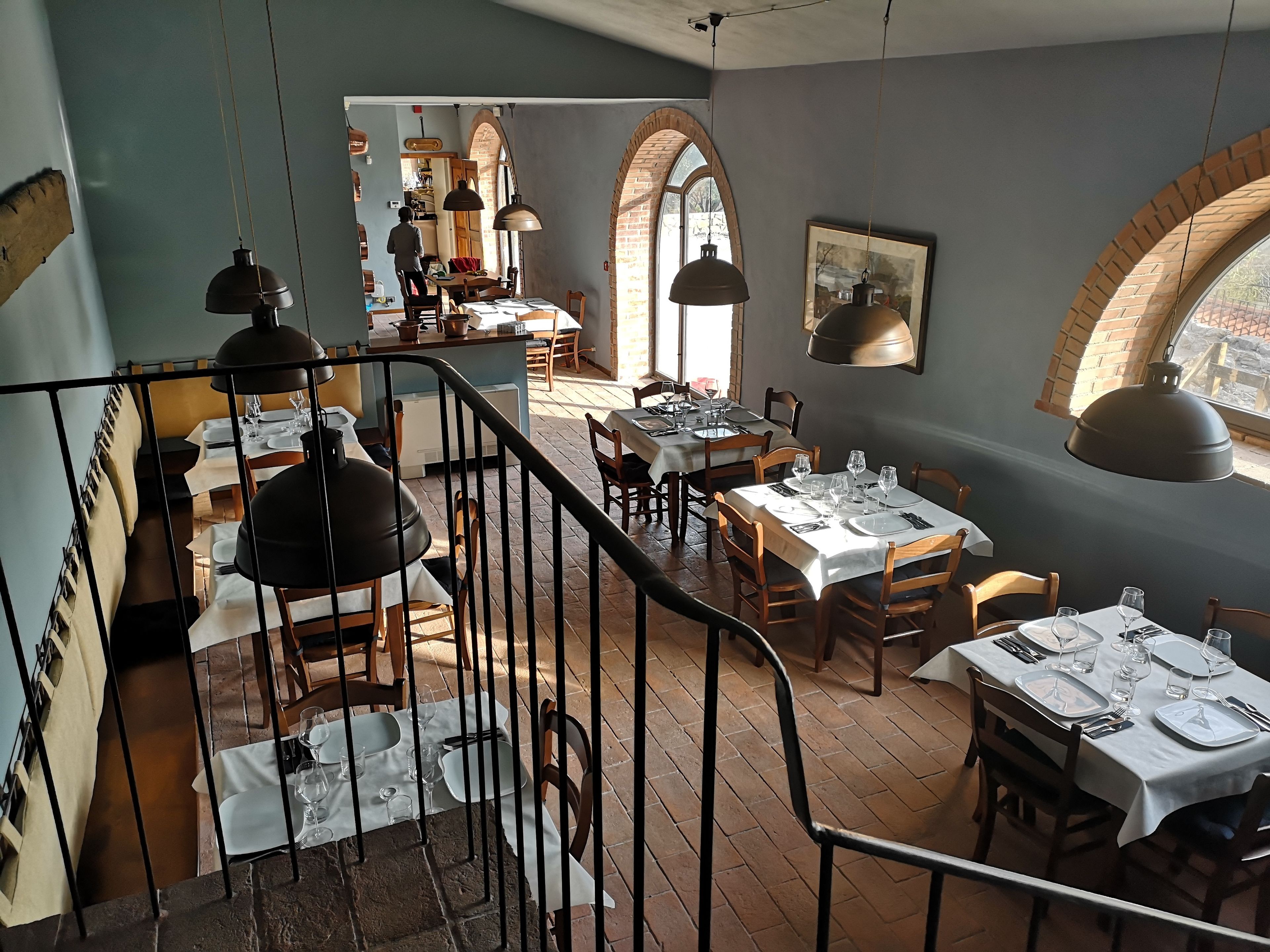 Ein Restaurant mit mehreren gedeckten Tischen für Gäste, das eine rustikale Backsteinwand und Rundbogenfenster zeigt.