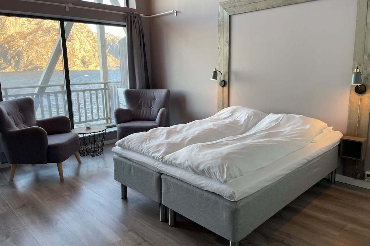 Un dormitorio moderno con una cama grande, dos sillones, una mesita y vistas al exterior a través de un amplio ventanal.