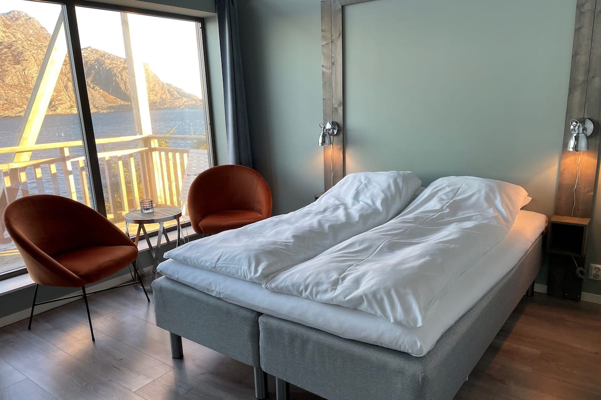 Un dormitorio moderno con una cama, dos sillones, una mesita y vistas a un puente y montañas.