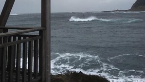 Une structure en bois surplombant une mer agitée, où les vagues s’écrasent sur le rivage.