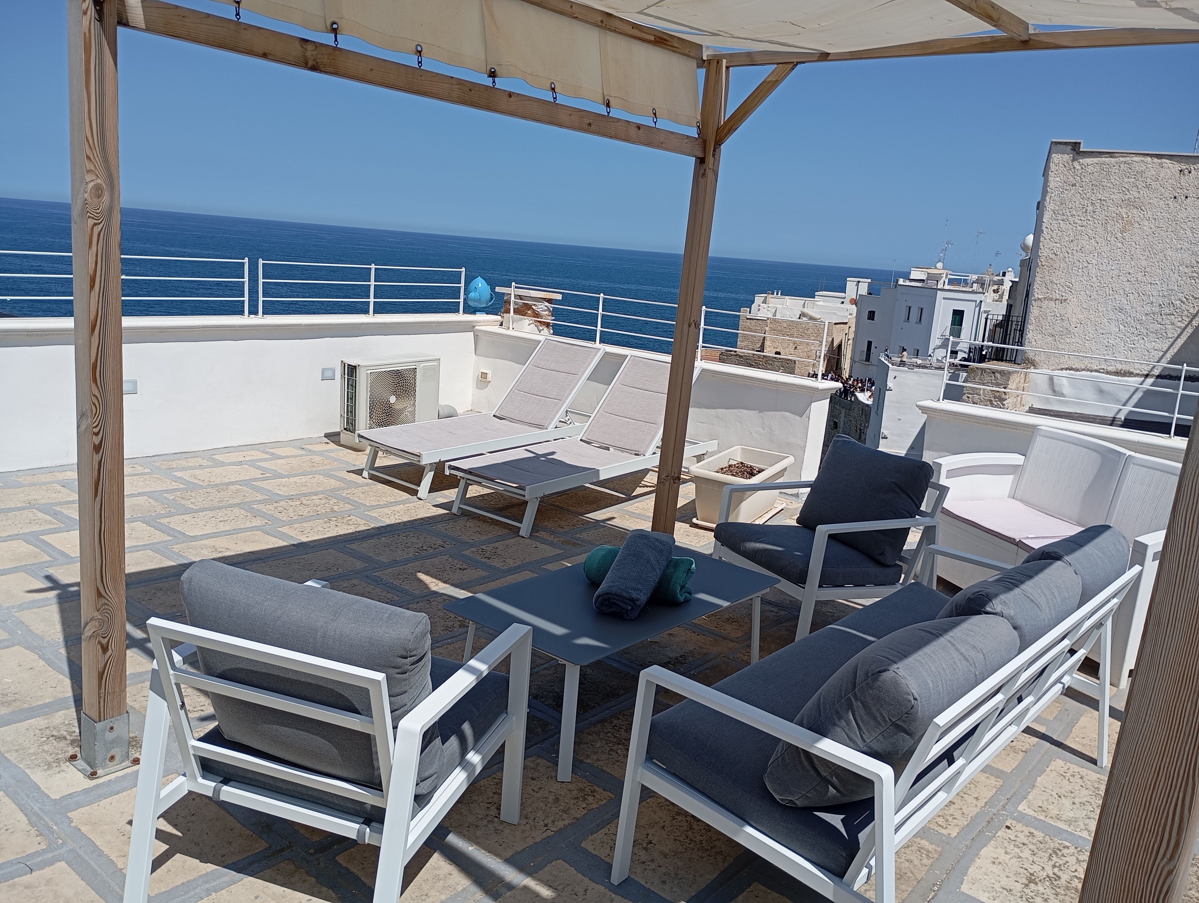 Una terraza en la azotea con mobiliario blanco, una pérgola y vistas al mar.
