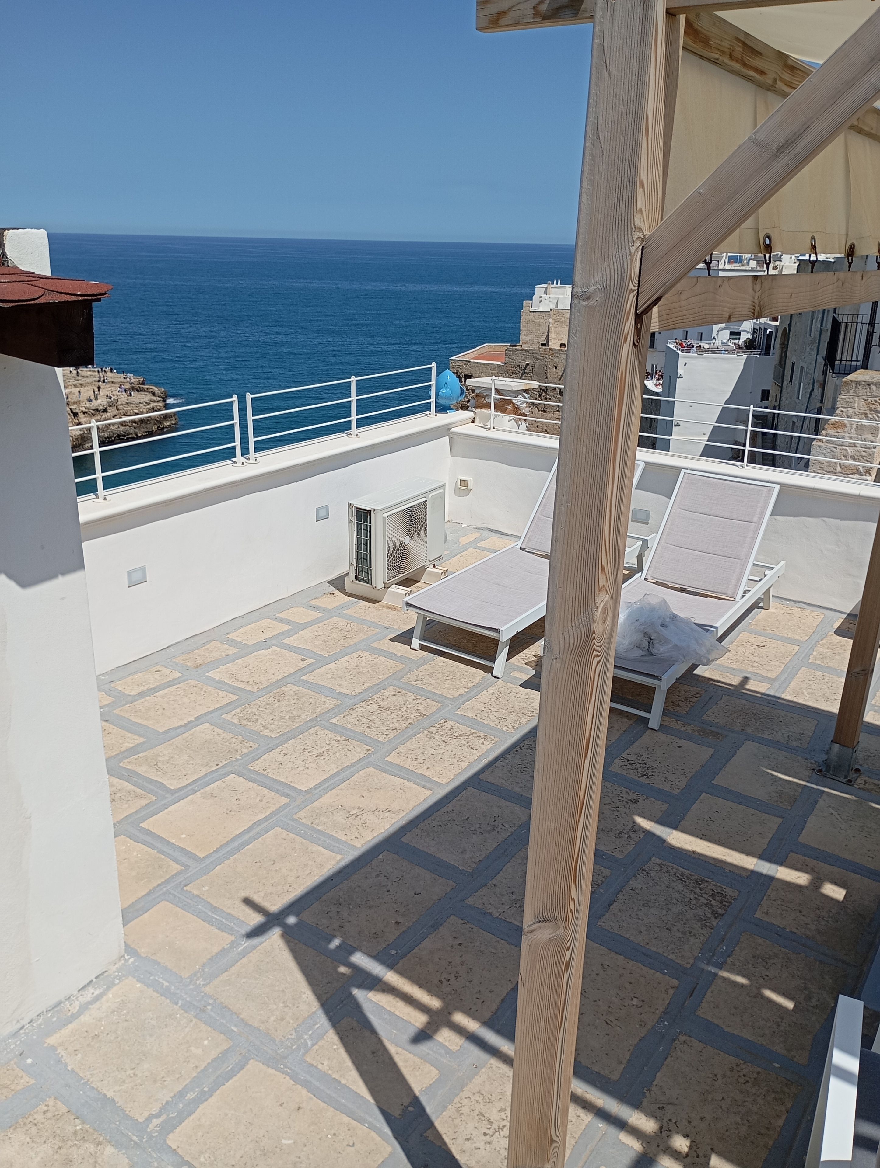 A rooftop terrace with a view of the sea, outdoor seating, and a stone floor.