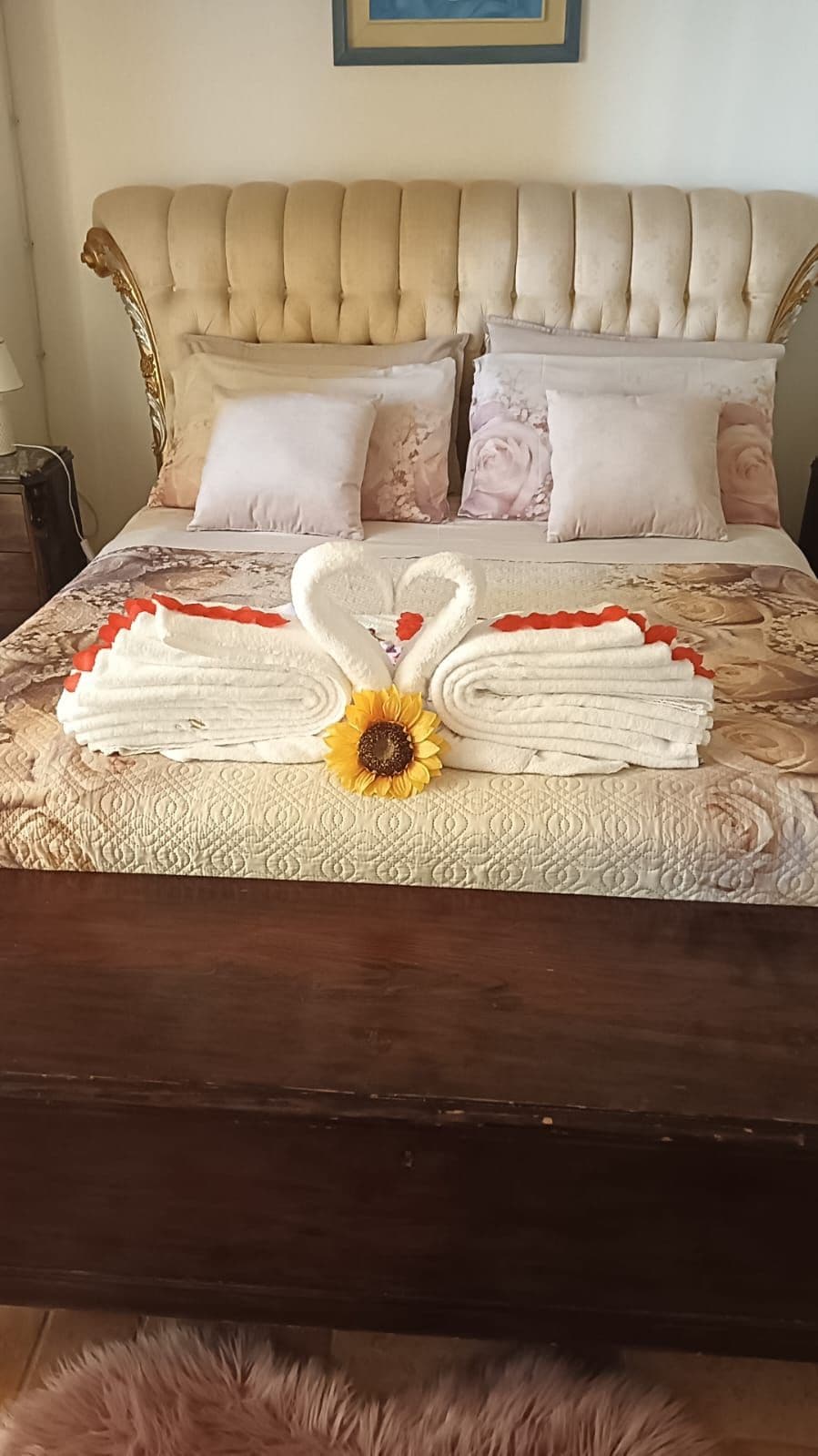 A bed with a headboard, pillows, and a decorative towel arrangement with a sunflower centerpiece.