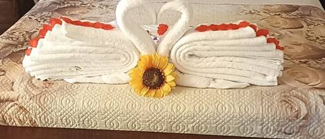 A bed with a headboard, pillows, and a decorative towel arrangement with a sunflower centerpiece.