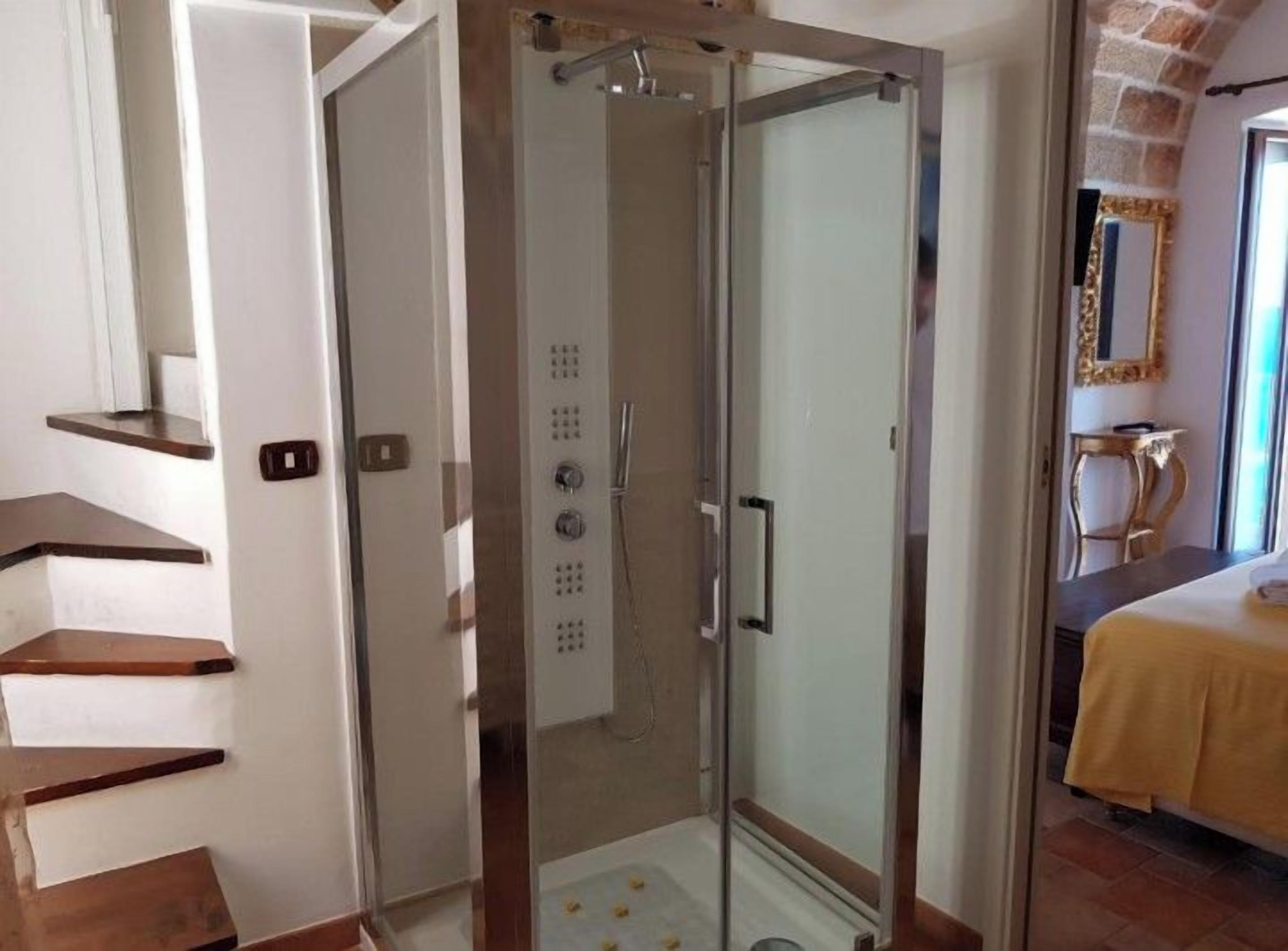 Une chambre d’hôtel avec une douche en verre, un lit recouvert d’une courtepointe jaune et un escalier avec des marches en bois.