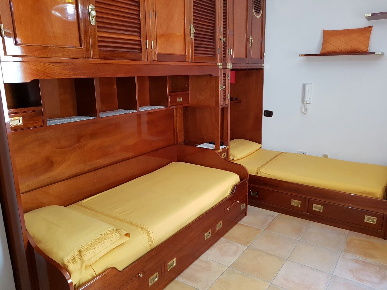 Ein kleines Zimmer mit zwei Holzbett, einem Einbauschrank und einem kleinen Regal.