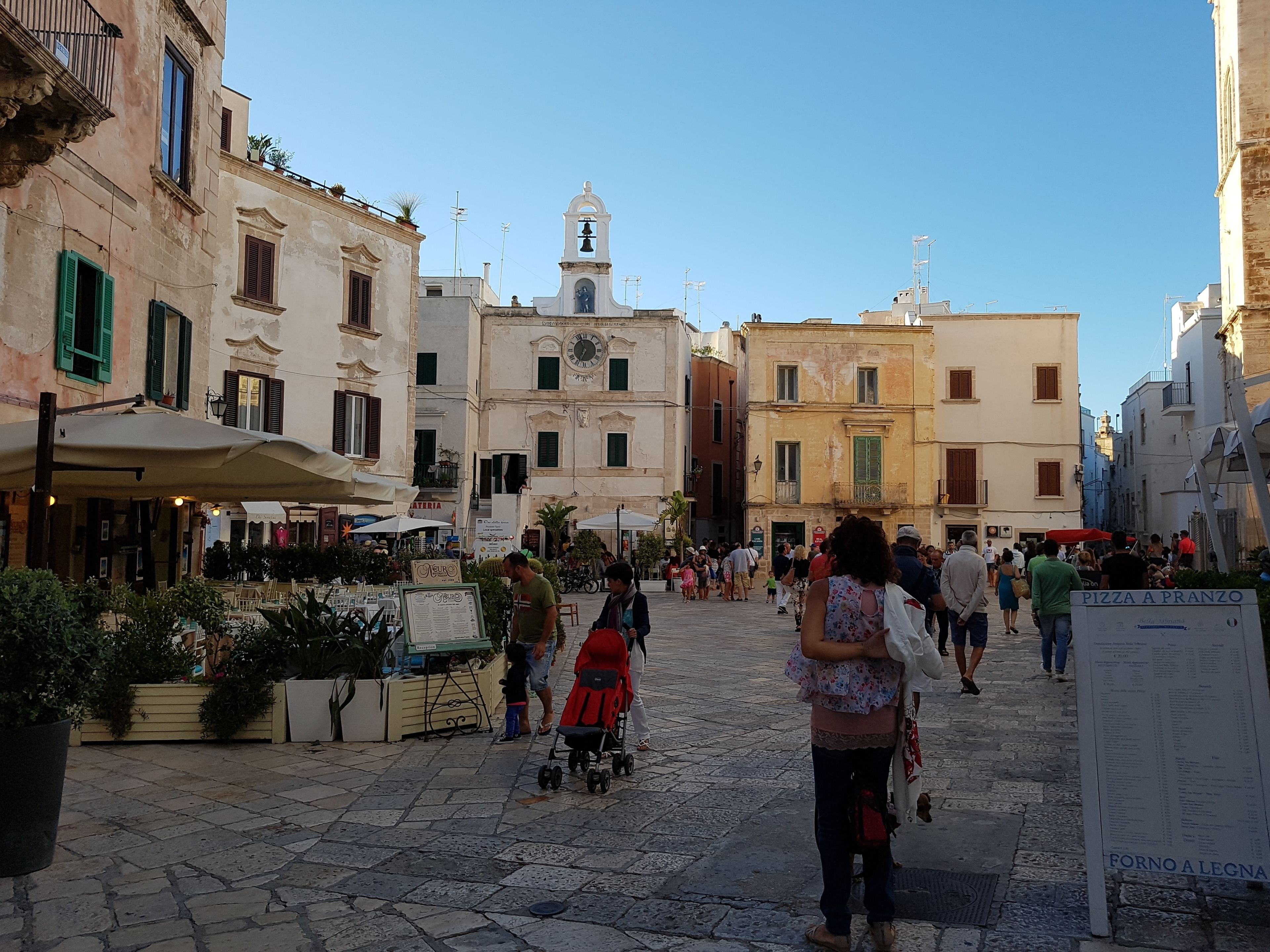 A cobblestone street with historic buildings, outdoor seating, and a clock tower.