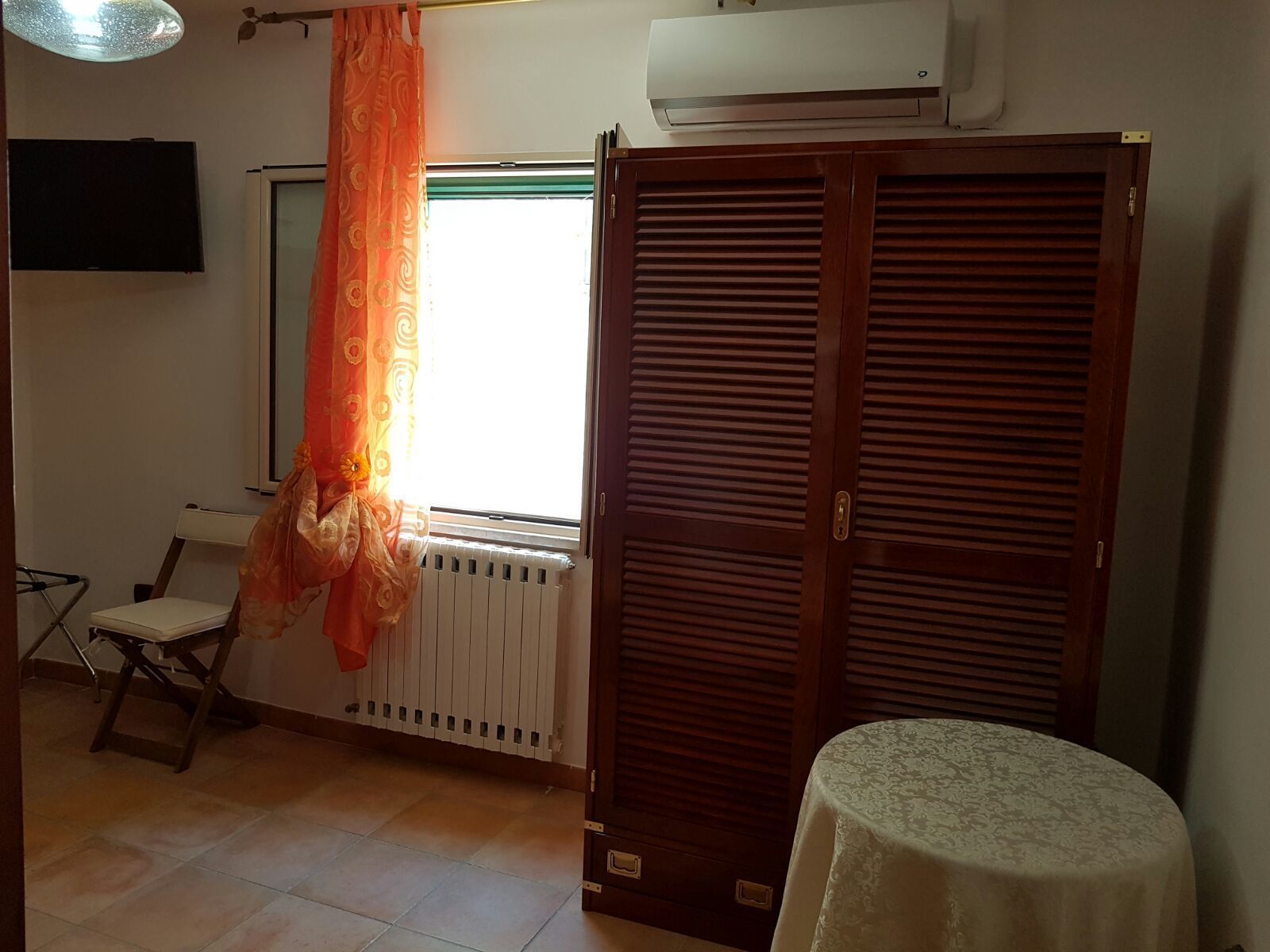 A room with a radiator, a wooden wardrobe, a table, and a chair.