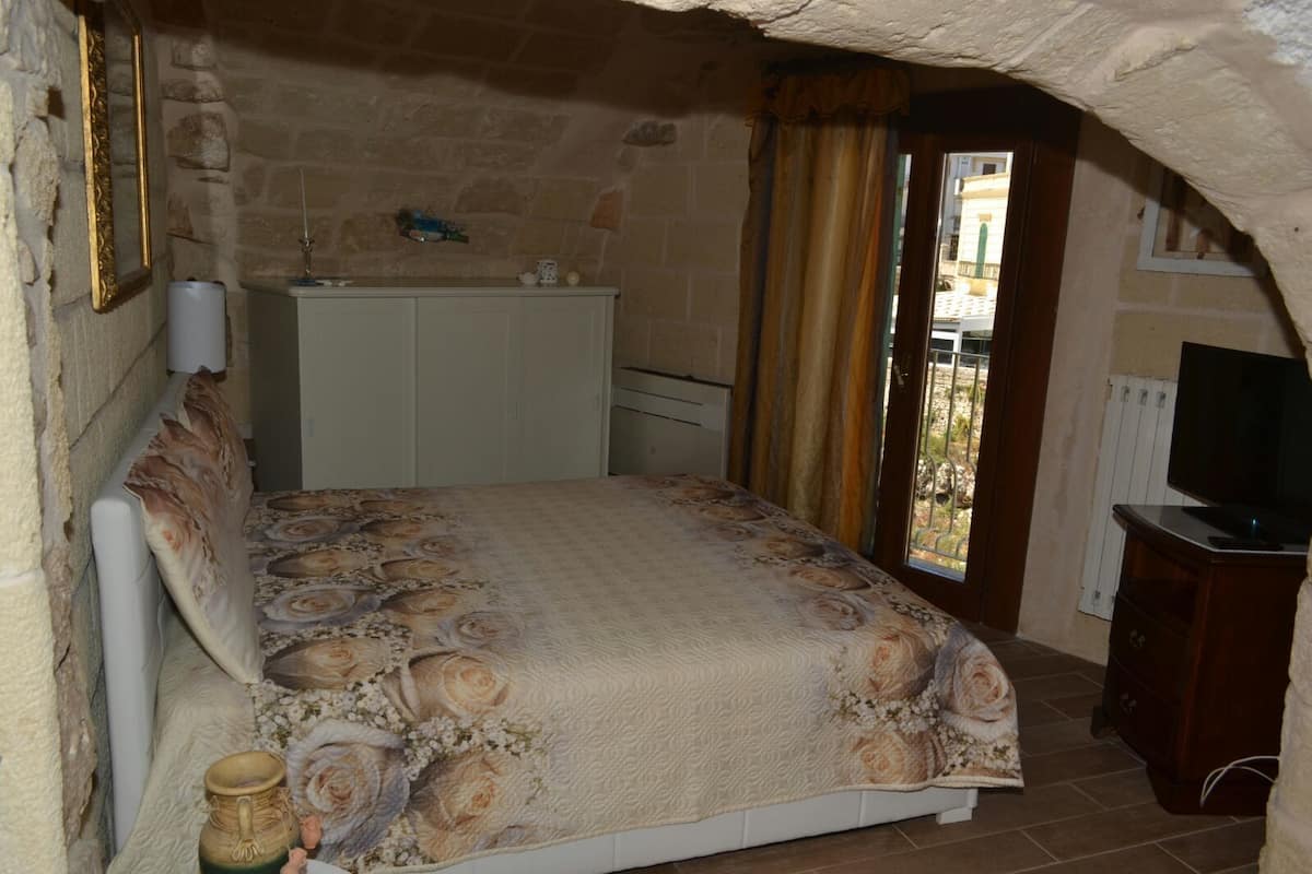 Quarto com cama, penteadeira, televisão e janela com cortinas.