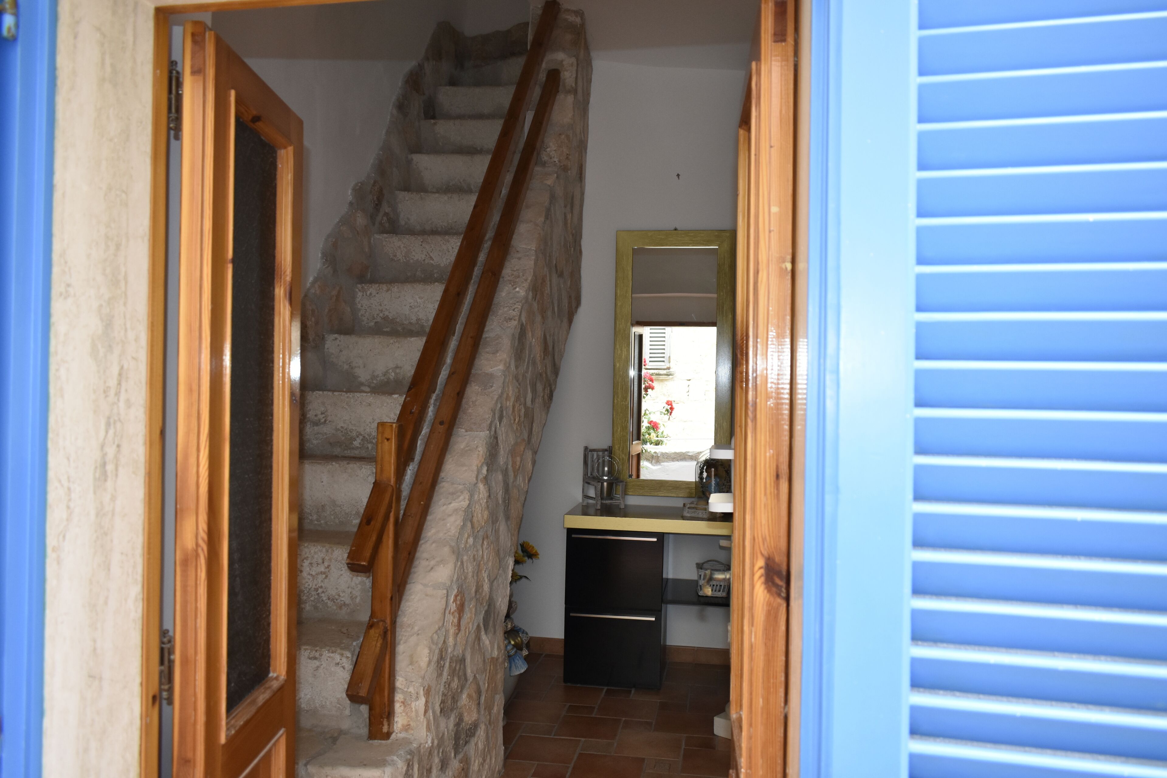 A staircase leading to a bedroom with a wooden handrail, a small desk with a mirror, and a window with blinds.
