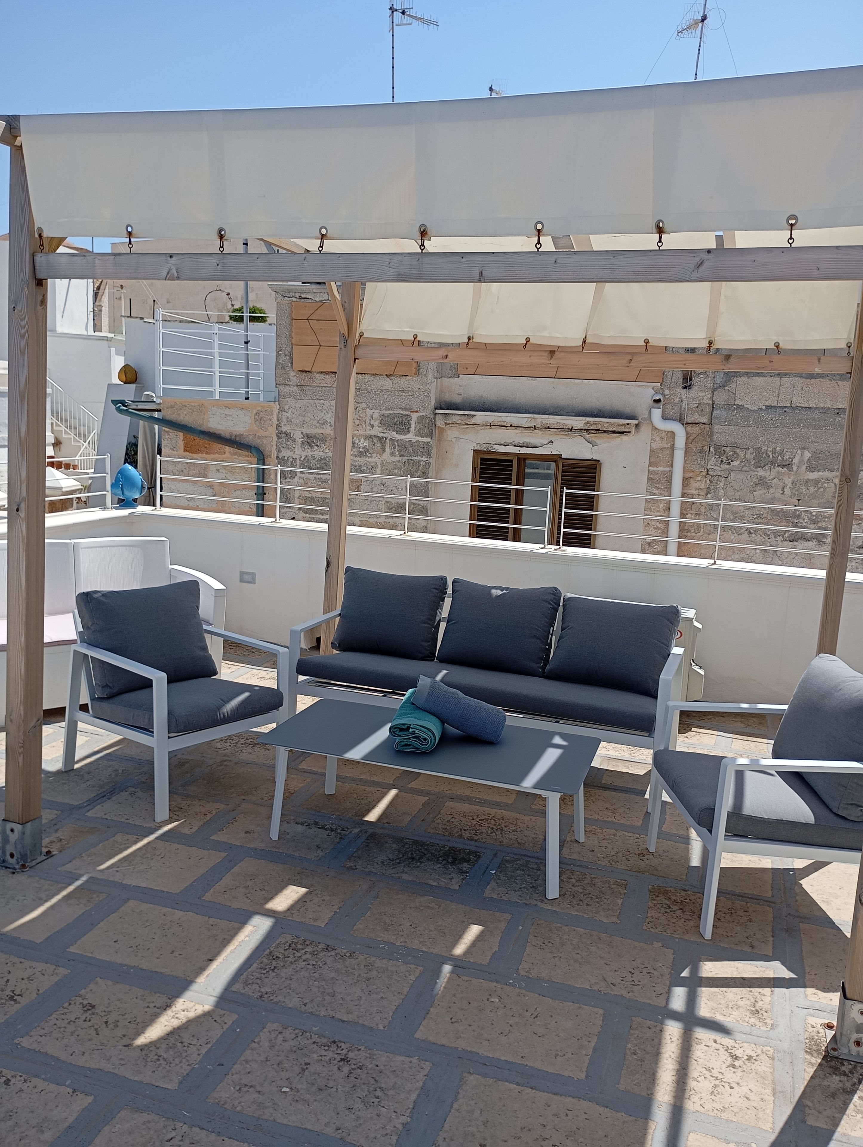 Un espace extérieur aménagé avec un canapé et des fauteuils, une table et une structure en forme de pergola.