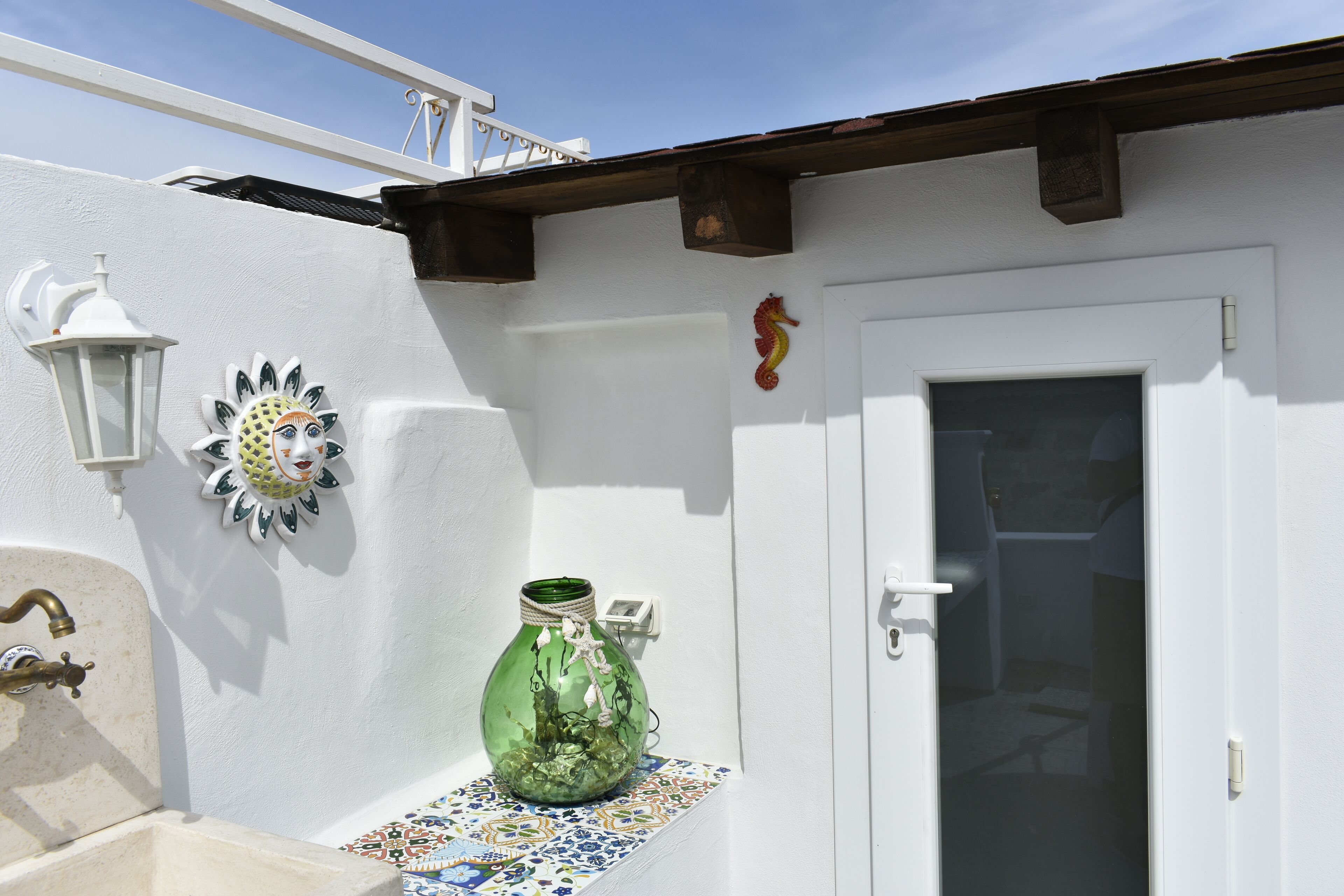 A white exterior wall with a decorative glass vase, a small window, and a door.