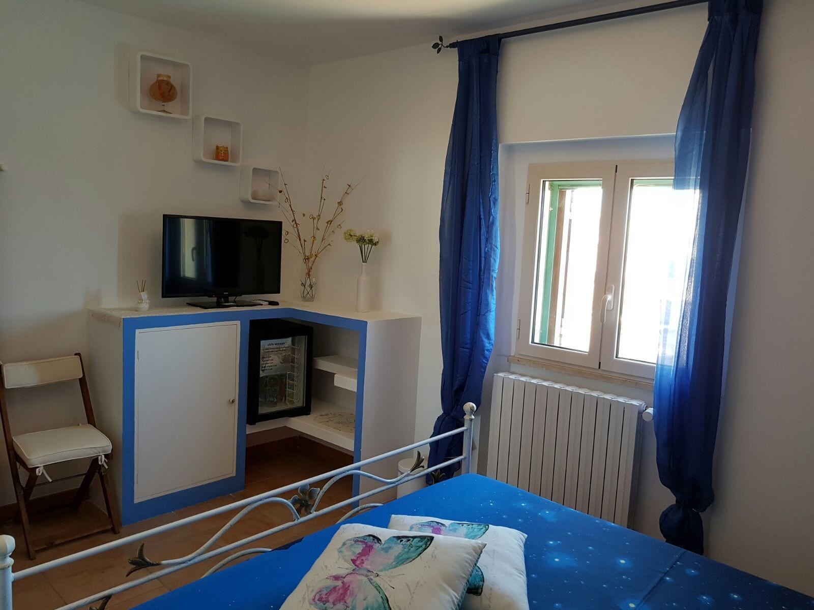 A bedroom with a bed, a TV, a desk, and a window with curtains.