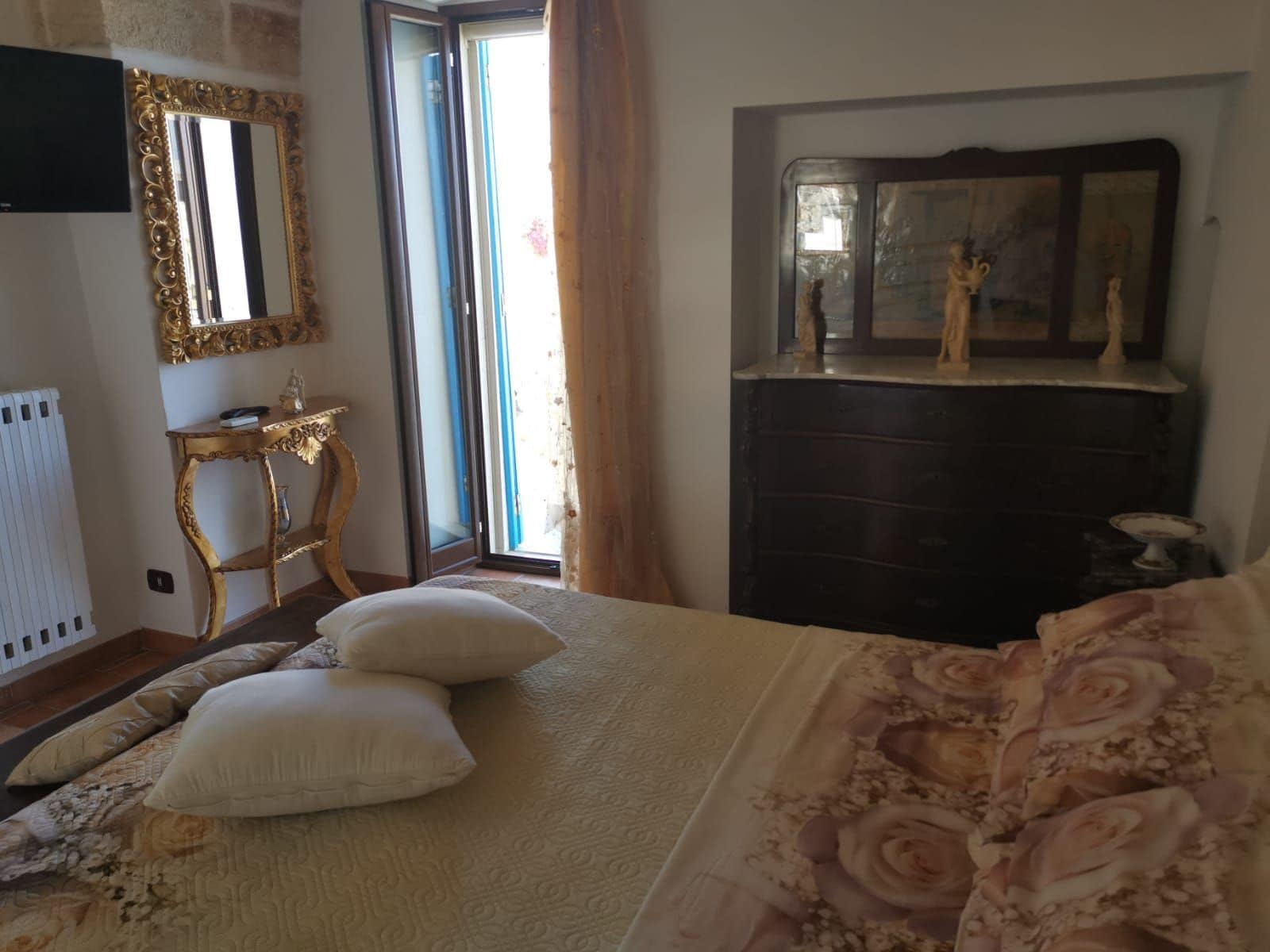 Un dormitorio con una cama, un aparador, un tocador con espejo y una ventana con cortinas.