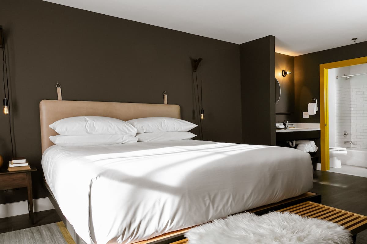 Un dormitorio moderno con una cama grande, mesitas de noche, una alfombra mullida y un baño con bañera y lavamanos.