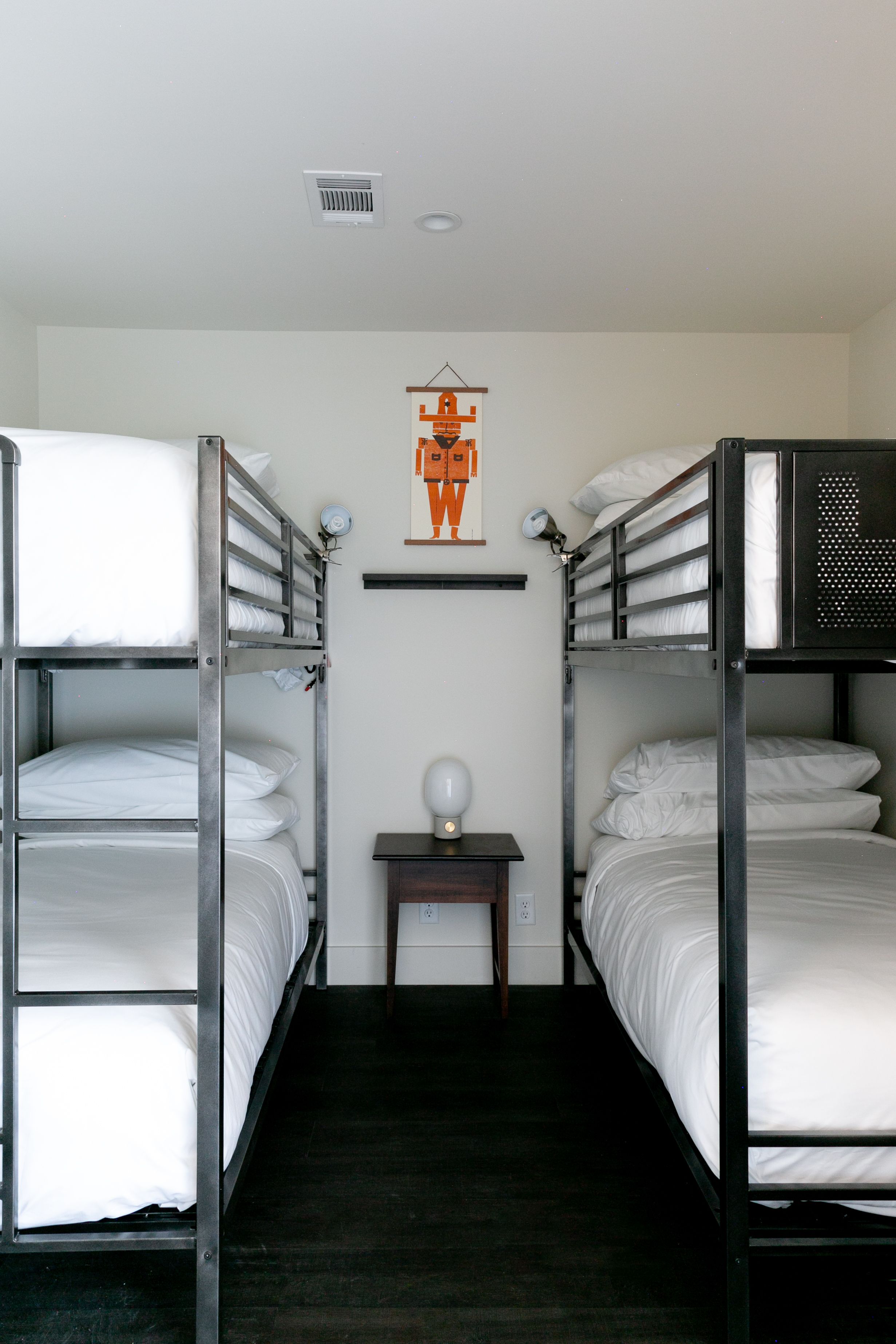 A bunk bed room with two beds, a small table with a lamp, and a poster on the wall.