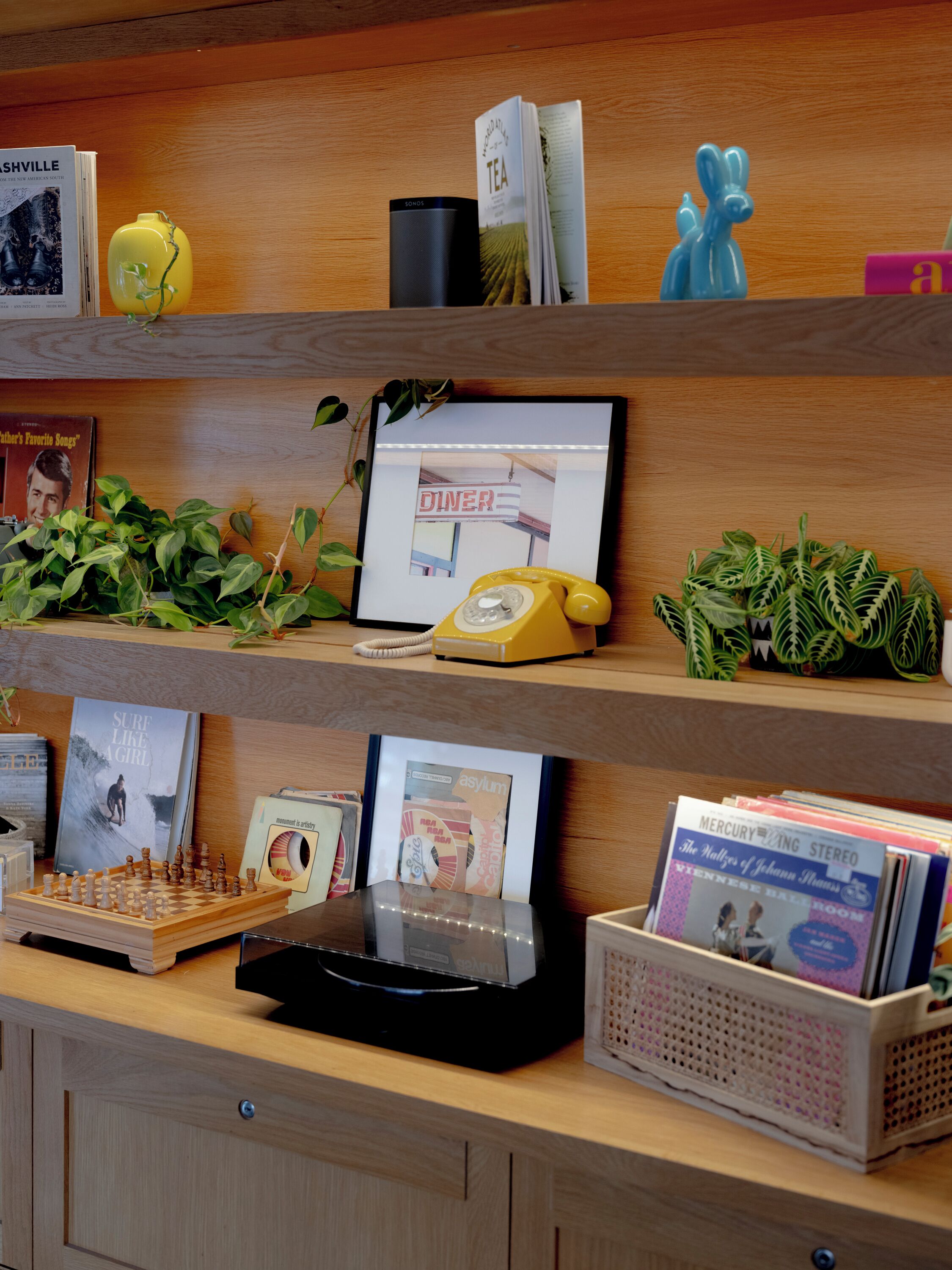 A wooden shelf with books, a yellow rotary phone, a framed picture, and a small potted plant.
