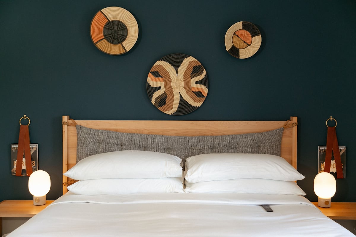 Una cama bien hecha con sábanas blancas, un cabecero de madera y dos lámparas de noche. Hay tres platos decorativos colgados en la pared sobre la cama.