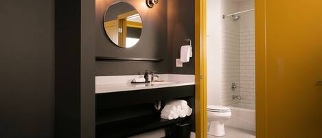 Un baño moderno con pared oscura, lavamanos blanco, espejo redondo, inodoro y bañera.