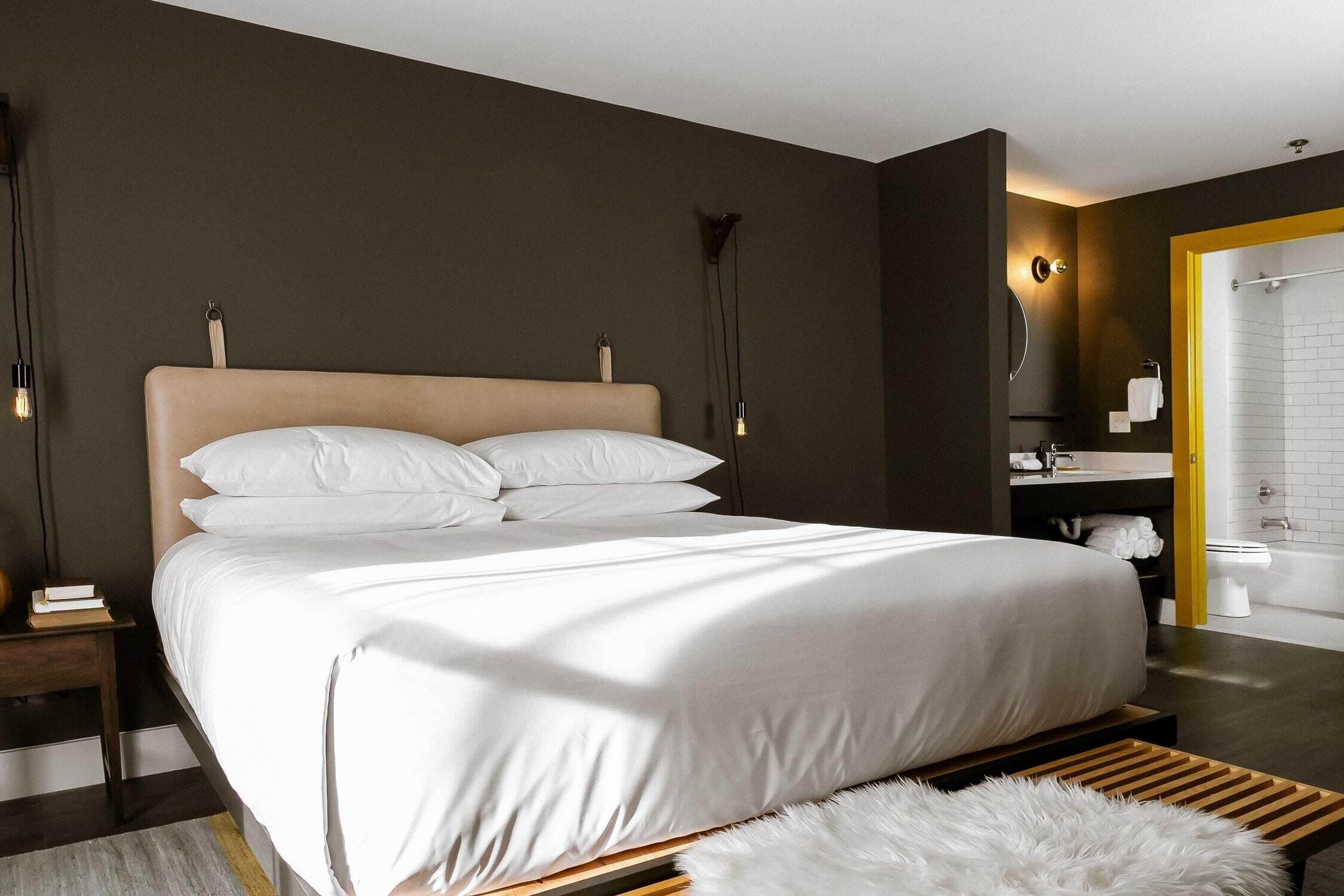 A modern bedroom with a large bed, bedside tables, a mirror, and a bathroom with a shower and toilet.
