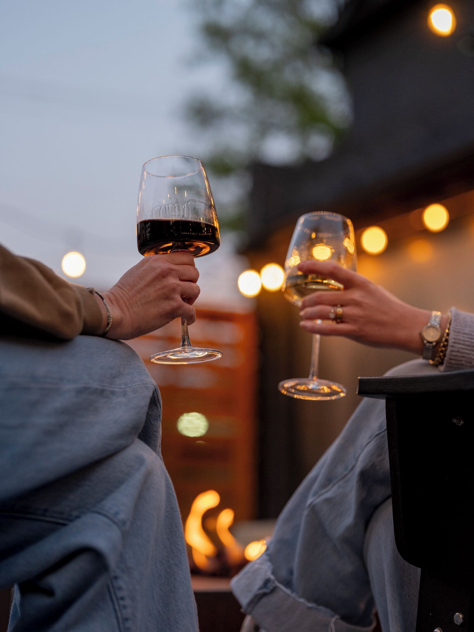 Dos personas brindando con copas de vino, una cálida chimenea al fondo y guirnaldas de luces.