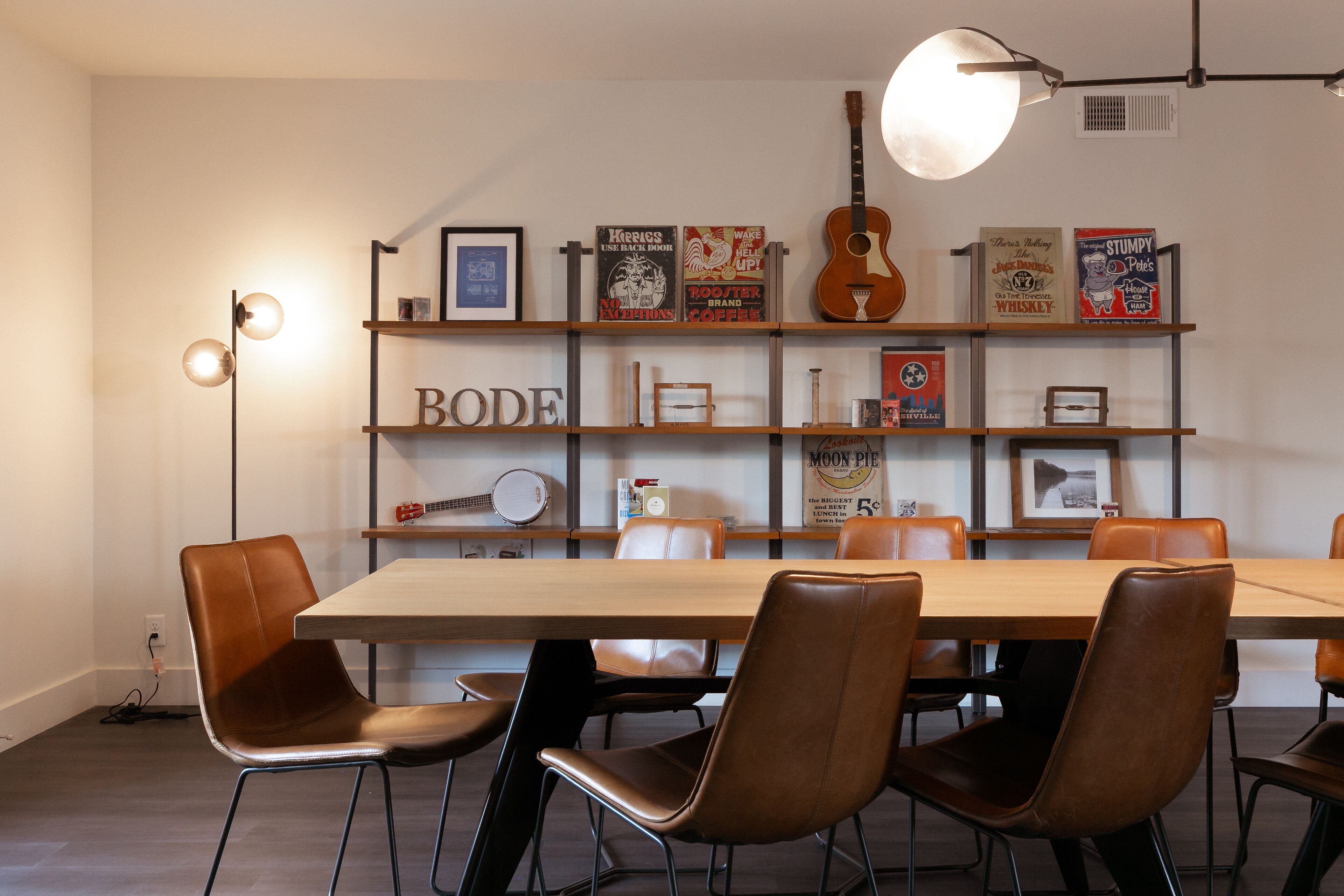 Un comedor con una mesa de madera y sillas de cuero marrón, una estantería con diversos objetos y una guitarra colgada en la pared.