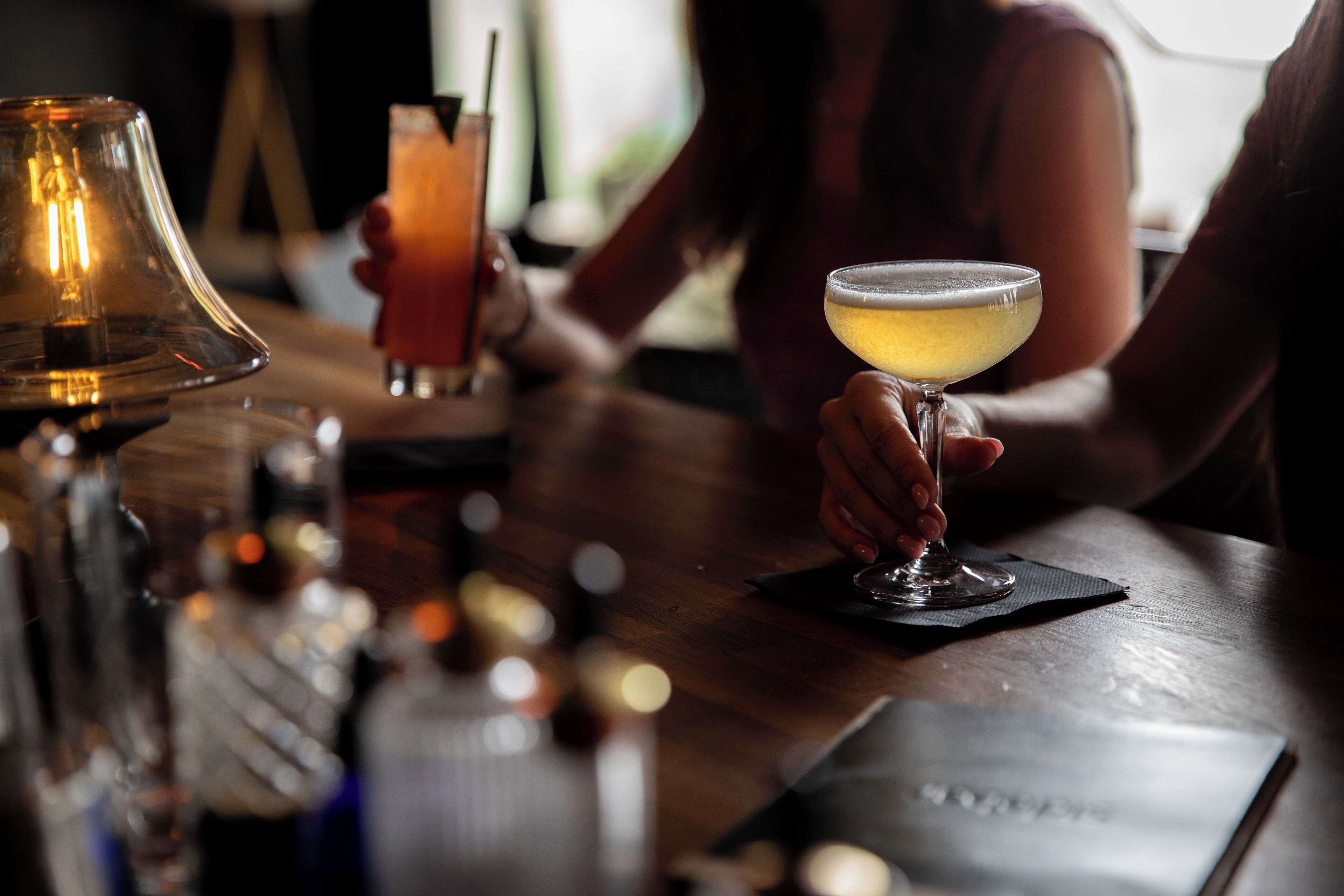 A bar setting with a glass of cocktail, a candle, and a bottle on the counter.
