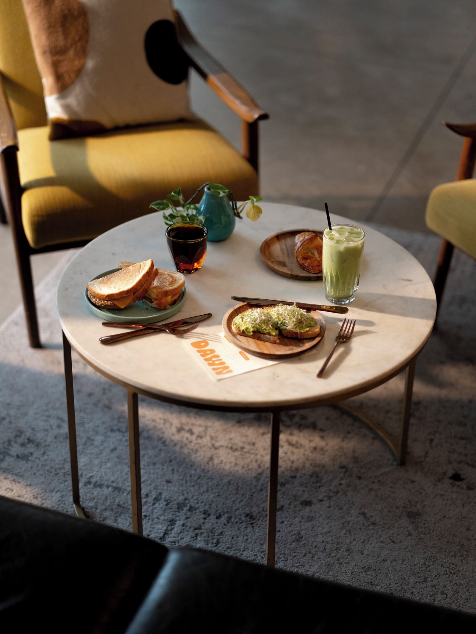 Una mesa redonda con un menú, una bebida y un sándwich.