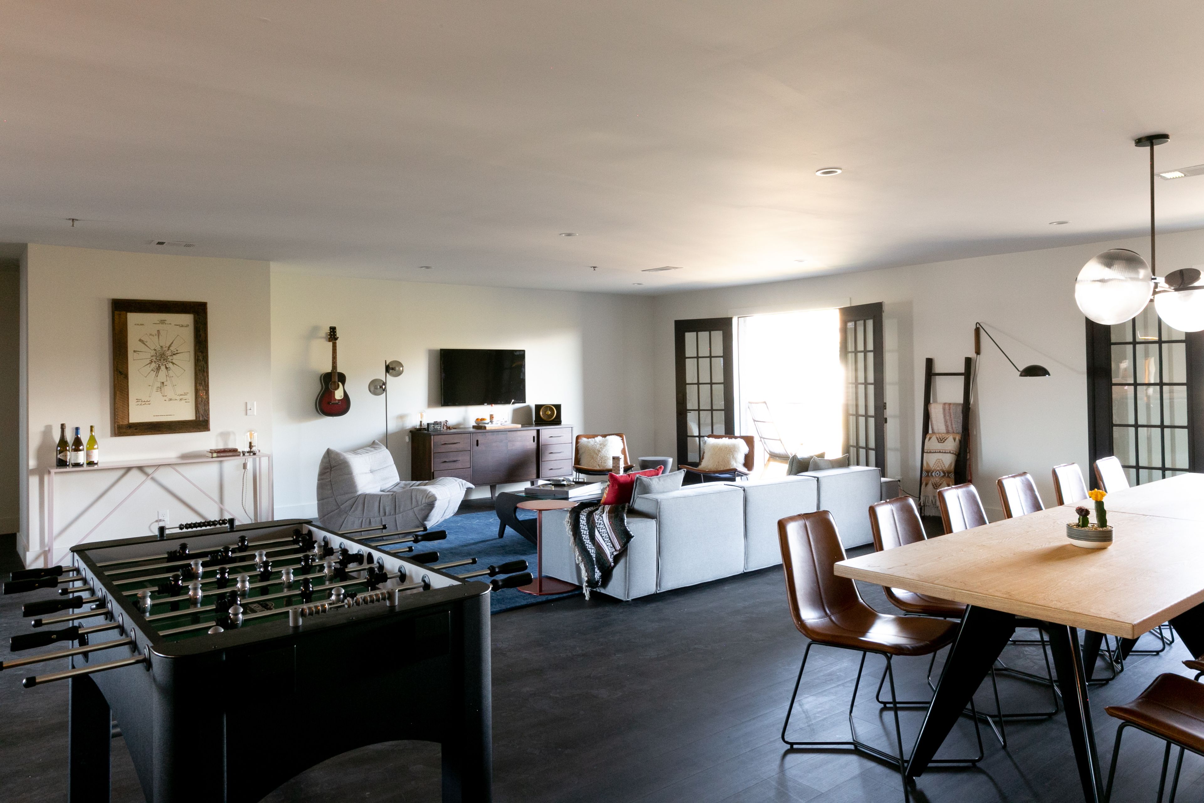 Amplia sala de estar con mesa de fútbol, sofá, mesa de comedor con sillas y área de cocina al fondo.