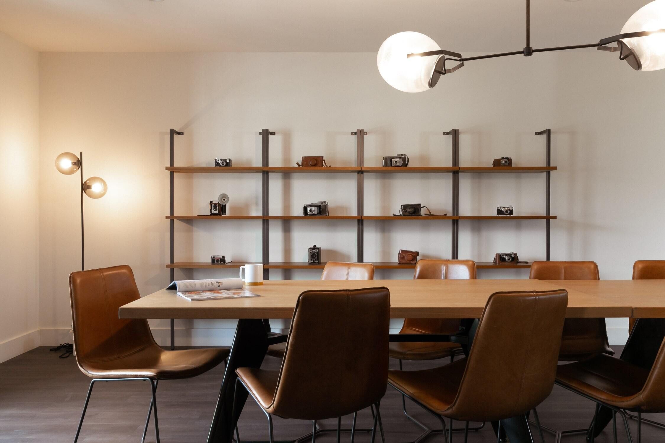 Une salle de conférence moderne, dotée d’une longue table, de six chaises et d’une étagère fixée au mur, sur laquelle sont disposées des caméras.