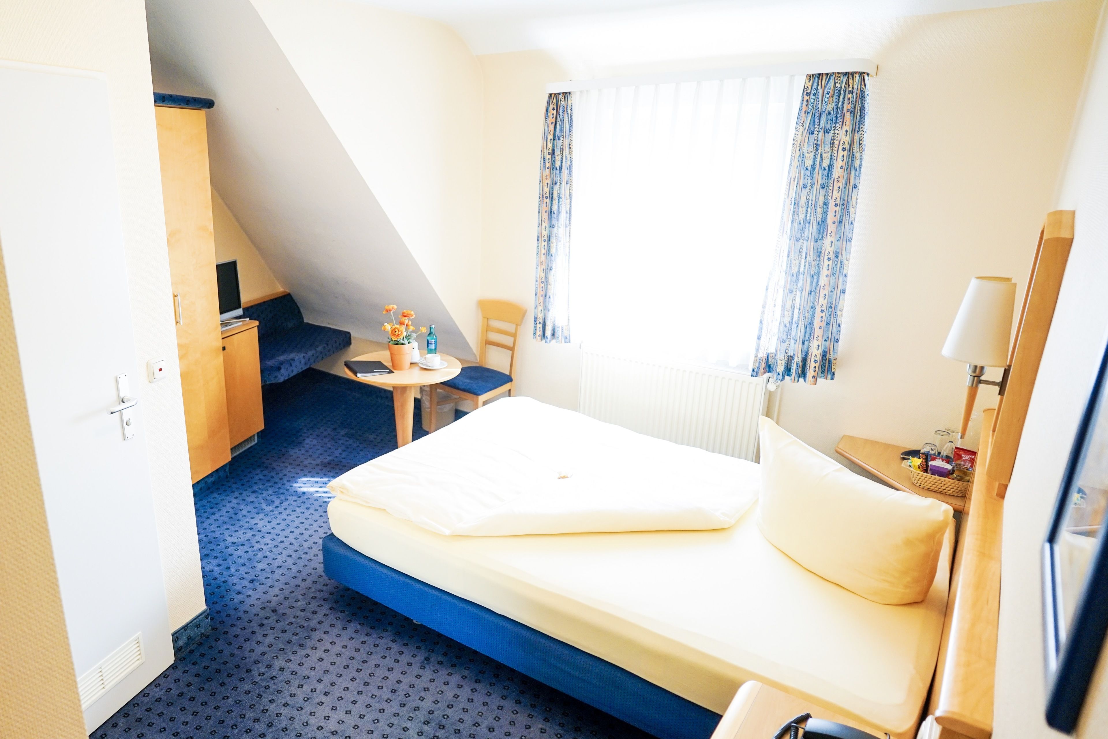 A hotel room with a bed, a desk, a chair, and a small table.