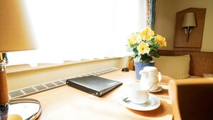 A hotel room with a wooden desk, a black notebook, a vase with yellow flowers, and a white teapot. - Hotel Sauer Garni (Neu-Isenburg)
