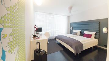 Habitación de hotel con cama, escritorio, silla, maleta y ventana con persianas.