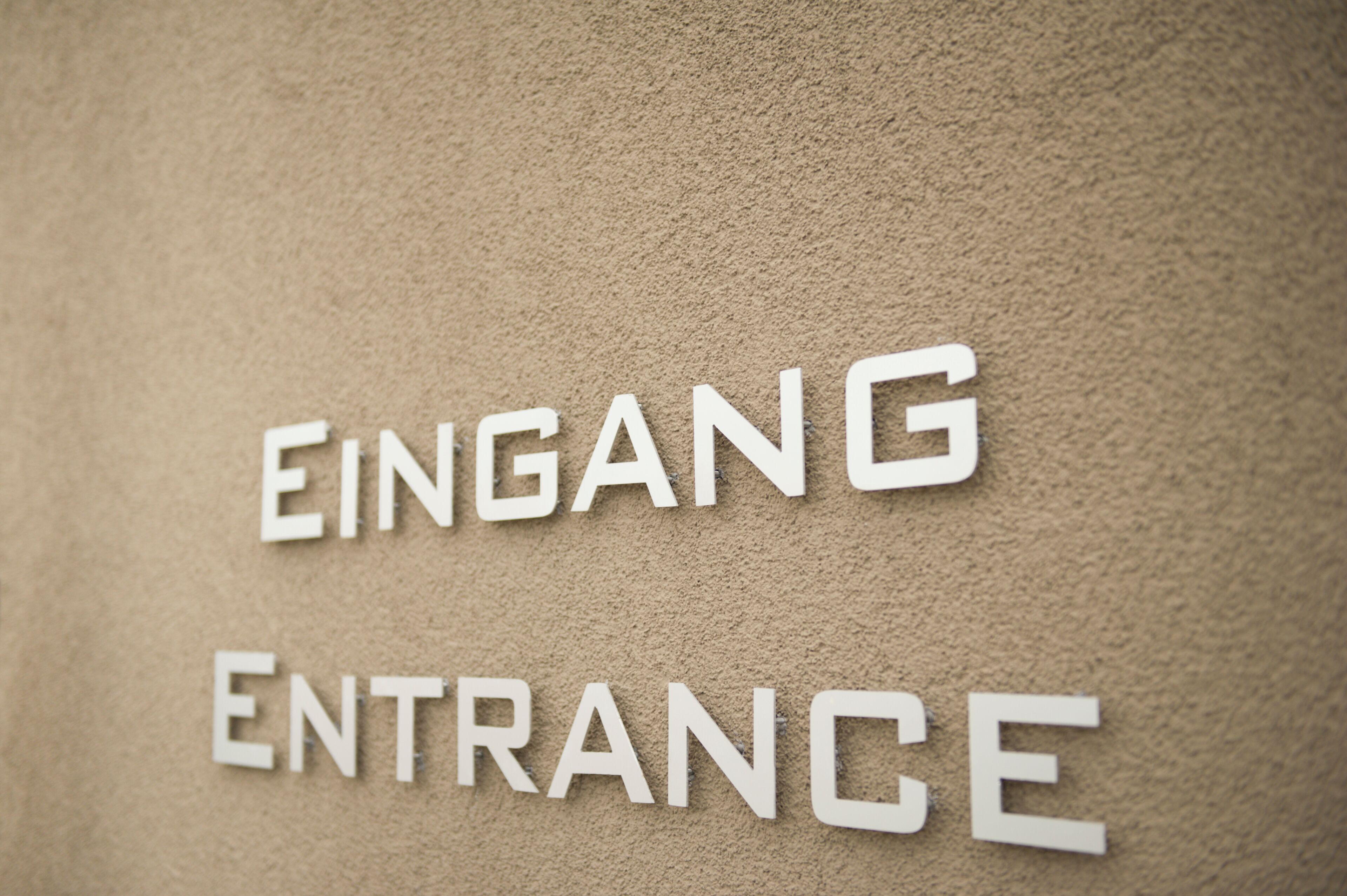 Un muro con le scritte 'EINGANG' e 'ENTRANCE' che indicano un ingresso.