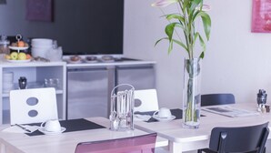 A modern dining area with a white table, black chairs, and a clear vase with green plants. - Sky Motel (Oberriet)